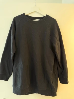 Svart sweatshirt från H&M - En enkel svart oversize sweatshirt från H&M i mjuk bomullsmix. Tröjan har rund halsringning, långa ärmar och ribbade muddar vid hals, ärmslut och nederkant. Perfekt för chill dagar eller när du vill ha en clean och basic look.