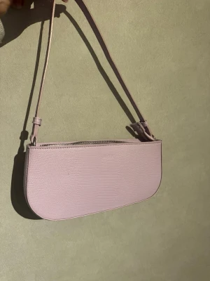 Ljuslila baugett/axelremsväska i skinnimitation - Supersnygg ljuslila baguetteväska i croco-liknande material 🤍 Perfekt storlek för mobil, plånbok och småsaker. Väskan har dragkedja med innerfack. Sparsamt använd och i väldigt fint skick – inga tydliga slitningar.