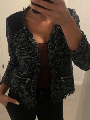 Svartvit cardigan jacka från Gina Tricot - Säljer en svartvit cardigan jacka från Gina Tricot med fransiga kanter och dragkedjedetaljer vid fickorna. Jackan är stickad med ett melerat mönster och har lång ärm. Perfekt för dig som vill ha en chill men ändå snygg look.