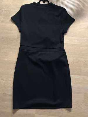 Svart kortklänning från H&M Divided - Säljer en svart kortklänning från H&M Divided i storlek L. Klänningen har korta ärmar, rund hals och en enkel, stilren design. Materialet känns mjukt och stretchigt, perfekt för dig som gillar minimalistisk stil.