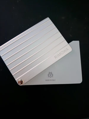 Rimowa Card-Holder - Säljer en stilren silverfärgad plånbok från Rimowa i metall med ett randigt mönster. Plånboken har en minimalistisk design och är tillverkad i Italien. Perfekt för kort och småsaker, med exklusiv känsla och snygg finish. Väldigt robust gjord av metall. Får plats perfekt i fickan och håller runt 6-8 kort. Köptes i Tyskland för 230€ motsvarande 2500kr och säljs för 1600kr. Finns att hämta på Östermalm. Snabb affär = 1400kr