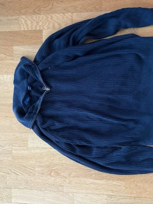 Marinblå ribbad tröja från GANT - Säljer en marinblå ribbad tröja från GANT med half zip-dragkedja vid kragen. Tröjan är långärmad och har en klassisk, lite loose passform. Perfekt för dig som gillar stilrena och bekväma plagg med snygg struktur.