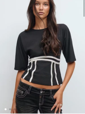 Svart topp  - Säljer en svart topp med vita dekorativa sömmar framtill och öppen rygg med knytband. Säljer för att den inte används💕pris kan diskuteras! slutsåld