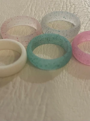 Fem färgglada ringar i silikon - Säljer ett set med fem ringar i silikon i olika färger: vit, ljusrosa, ljusblå, blå och rosa. Några av ringarna har glittereffekt som ger en extra touch. Perfekta för att mixa och matcha till din stil.
