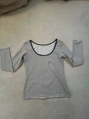 Randig långärmad topp med rund hals - Säljer en vit och svart långärmad topp med smala horisontella ränder och rundad halsringning. Toppen har en slim passform och är tillverkad i ett mjukt och stretchigt material som sitter snyggt på kroppen. Perfekt att styla med jeans eller kjol. 