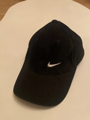 Svart keps - En svart, justerbar, keps med en broderad logga av nikemärket. 