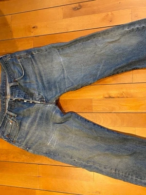 Levi's 501 jeans blå W34 L32 - Klassiska Levi's 501 jeans i blå tvätt med raka ben och knappgylf. Jeansen har fem fickor, tydliga kontrastsömmar och den ikoniska läderpatchen bak i midjan. Materialet är slitstark bomull och passformen är straight. Perfekt för dig som gillar tidlös denimstil.