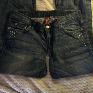 Divide bootcut jeans med nitar - Snygga blå jeans i klassisk denim med fina strass-/nitar på framfickorna som ger en extra detalj ✨ Jeansen har en lätt tvättad look och passar perfekt till både vardag och fest. Sköna och stilrena – enkla att matcha med topp, hoodie eller jacka. I bra skick 85cm i innerbenslängd. 39cm tvärs över midjan