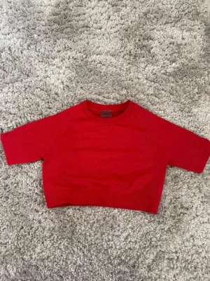 Röd croppad topp från Aimn - Säljer en röd croppad topp från Aimn med korta ärmar och ribbad nederkant. Toppen har en enkel design utan mönster och är tillverkad i mjuk bomull. Perfekt för dig som gillar sportiga och stilrena plagg. Aldrig använd! Var snabb med att ta bort prislappen.