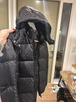 Svart mönstrad jacka från Boss - Säljer en svart pufferjacka från BOSS i storlek XS med snyggt geometriskt mönster. Jackan har huva, dragkedja och är fodrad med beige och vit insida. Perfekt för kalla dagar när du vill vara både varm och stilren.