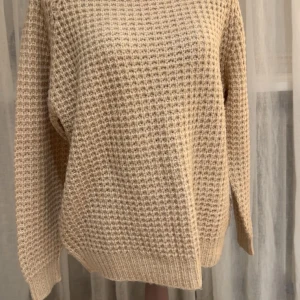 Beige stickad tröja med struktur - Säljer en beige stickad tröja med grov struktur och rund hals. Tröjan har lång ärm och ribbade muddar vid hals, ärmslut och nederkant. Den är jätte mjuk och skön