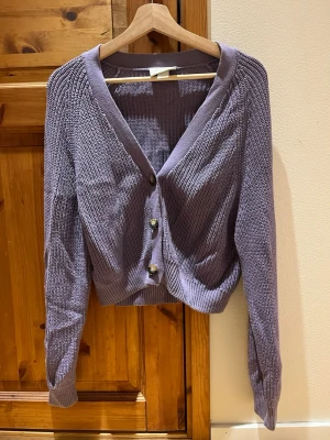 Lila Monki kofta - Lila kofta från Monki i storlek XS. Kan upplevas något kortare i midjan. Knäppe med 3st bruna knappar i mitten. Vid knäppning kan koftan upplevas i vissa fall lite V-ringad. Bra skick, sparsamt använd. Säljes då den inte kommer till användning. Djur och rökfritt hem.