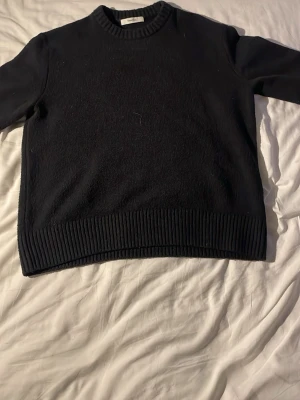 Svart stickad tröja. - Säljer en svart stickad med rund hals och breda ribbade muddar vid nederkant och hals. Tröjan har lång ärm och är i mjukt material som passar perfekt för kyliga dagar. Enkel och stilren design som funkar till många outfits. Använd typ 2 ggr och säljer då den är för stor för mig. Pris går o diskutera.