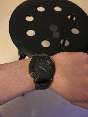 Svart G-Shock klocka med resinband - Säljer en svart G-Shock Casio klocka med digital och analog display. Klockan har ett transparent resinband och robust design med metallspänne. Perfekt för dig som gillar en stilren och tålig accessoar. Vattentät till 20 bar och har bakgrundsbelysning.