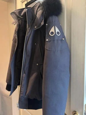 Svart Moose Knuckles Ballistic Bomber Puffer - Säljer en svart pufferjacka från Moose Knuckles med svart päls på luvan.  Köpt från vestiaire collective i sommras och har använts kanske 3-4 gånger. Digitalt kvitto kan visas.