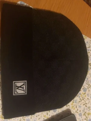 Svart mössa med vit logga  - Svart mössa med vit logga, den passar hela outfit speciellt till vinter eller vår. Den är ny!! 