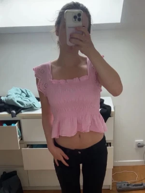 Rosa blus med volang  - Söt ljusrosa blus med smockad midja, volang nertill och knytband i ryggen. Bra skick 