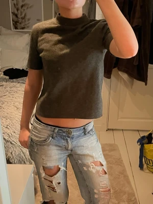 Mörkgrå croppad t-shirt från Zara - Snygg mörkgrå croppad t-shirt från Zara med korta ärmar och hög hals. T-shirten är i mjukt bomullsmaterial och har en clean, minimalistisk look som är enkel att matcha med jeans eller kjol. Perfekt för dig som gillar stilrena plagg med modern passform🫶🏼