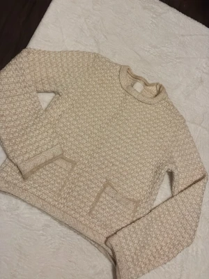 Beige stickad tröja från H&M XS - Säljer en beige stickad tröja från H&M i storlek XS. Tröjan har ett grovt, strukturerat mönster och två praktiska fickor framtill. Rund hals och långa ärmar ger en chill och mysig vibe. Perfekt för lager-på-lager under kyliga dagar.