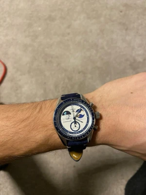 Omega X Swatch Moonswatch Metal Case - Omega X Swatch Moonswatch Mission to Earthphase Moonshine Gold Snoppy i Metall Case. Väldigt unik och stilren klocka, följer med boxen och original case + armband. Armbandet som är på just nu är justerbart och gjord i mörkblå mocka/suede.