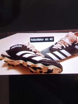 Adidas Predator fotbollsskor strl 40 - Säljer ett par svarta och vita Adidas Predator fotbollsskor i storlek 40. Skorna har klassiska tre ränder på sidan, snörning och mönstrad ovansida för extra grepp. Sulan har dobbar för bra fäste på planen. Perfekt för dig som vill ta ditt spel till nästa nivå.
