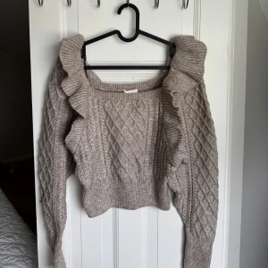 Beige stickad tröja med volang  - Superfin beige stickad tröja från H&M i storlek XS. Tröjan har ett snyggt kabelstickat mönster, långa ärmar och coola volangdetaljer längs axlarna. Perfekt för dig som gillar en söt men trendig look. Aldrig använd 