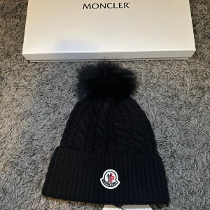 Moncler vintermössa dam - NFC tag, oanvänd, original, box + påse tillgänglig  - Säljer en äkta Moncler mössa för dam i oanvänt skick Klassisk modell med Moncler logotyp, framtill, tillverkad i mjuk ullblandning som håller värmen väldigt bra Inga noppor, fläckar eller andra skador Färg: Svart Storlek: One Size Material: Ullblandning Äkta vara - logotyp, etikett, påse, nfc tag och box stämmer överens med original Kommer från rök- djurfritt hem Skickas noggrant förpackad inom någon timme efter köp 
