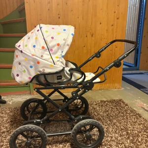 BRIO barnvagn med prickigt tyg - Söt BRIO barnvagn med färgglatt prickigt tyg. Stabil ram, stora hjul och justerbart handtag. Tyget är i fint skick utan synliga fläckar eller revor. Passar perfekt för dockor eller små barn. Något slitage på hjulen, men överlag mycket bra skick.