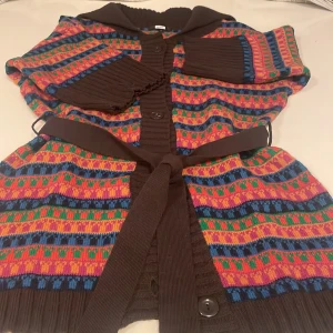 Färgglad kofta från BIK BOK med bälte - Säljer en unik kofta från BIK BOK i storlek S med färgglada ränder. Koftan har bred krage, knappar framtill och ett matchande bälte i midjan. Stickad känsla och kortare ärmar med ribbade muddar ger en cool och mysig vibe.