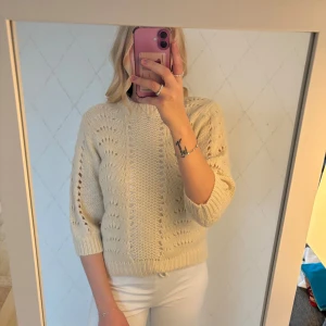 Beige stickad tröja med hålmönster - Superfin beige stickad tröja med snyggt hålmönster och ribbade muddar. Tröjan har trekvartsärm och en lite lösare passform, perfekt för lager på lager. Mjuk och mysig, passar till både jeans och kjol.