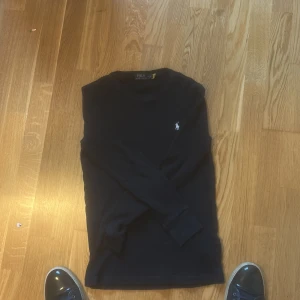 Mörkblå långärmad tröja Polo Ralph Lauren - Mörkblå långärmad tröja från Polo Ralph Lauren med klassisk broderad logga på bröstet. Tröjan är ribbstickad och har en rund halsringning. Perfekt för dig som gillar stilren och tidlös design. Den är använd ett få antal gånger.