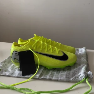 Nike Mercurial Air Zoom fotbollsskor - Säljer ett par grymt snygga Nike Mercurial Air Zoom fotbollsskor i neon-gul med svarta detaljer. Skorna har snörning, platt sula med dobbar och Dynamic Fit-teknologi för extra komfort. Ovandelen är tillverkad i syntetmaterial med ventilerande mesh och cool design.