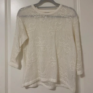 Vit spetsblus med trekvartsärm - En vit blus i spets med mönster och trekvartsärmar. Blusen har rund halsringning 