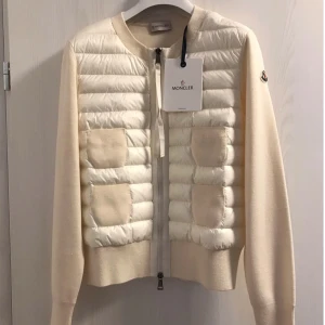Beige cardigan jacka från Moncler - Snygg beige cardigan jacka från Moncler med quiltad front i ljusbeige och fyra stickade fickor. Jackan har ribbad krage, långärmade stickade ärmar och dragkedja framtill. Perfekt för dig som gillar stilren design och exklusiva detaljer. Helt ny! (Kan tänka mig byta till exakt likadan fast i svart)💓