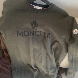 Mörkgrön sweatshirt från Moncler - Snygg mörkgrön sweatshirt från Moncler med broderad logga på bröstet och patch på ärmen. Tröjan har rund hals, långa ärmar och ribbade muddar. Perfekt för dig som gillar stilrena och exklusiva plagg med streetkänsla.