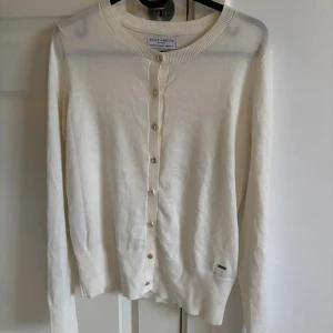 Vit kofta från Holly & Whyte - Vit kofta från Holly & Whyte med guldiga knappar framtill. Använd fåtal gånger och säljer då den inte kommit till användning💕