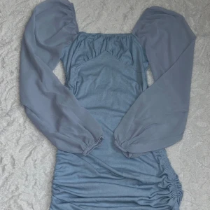 Ljusblå kortklänning från SHEIN - Supersöt ljusblå kortklänning från SHEIN med puffiga långärmar i transparent tyg och ribbad kropp. Klänningen har rynkade detaljer på sidan och en fyrkantig urringning. Skriv vid frågor 🥰