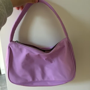 Ljuslila axelväska med dragkedja - Snygg axelväska i ljuslila färg med enkel, stilren design. Väskan har en bred axelrem och stängs med dragkedja upptill. Perfekt storlek för det viktigaste och ger en poppig touch till din outfit. Aldrig använd! 🩷