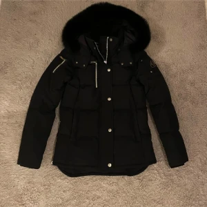 Svart jacka från Moose Knuckles - Säljer min systers korta variant av moose knuckles jacka. Den är i bra skick men har ett litet hål på sidan som knappt syns. Pälsen är avtagbar. Användes en vinter sen har den bara legat och dammat i garderoben och därav har min syster även ej hållt koll på kvittot.