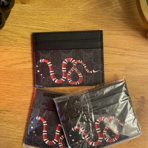 Svart kortfodral med röd orm - Snyggt svart kortfodral med ett coolt ormmotiv i rött, vitt och svart. Perfekt för dig som vill ha något unikt och stilrent till dina kort. Fodralet har flera fack och är gjort i tåligt syntetmaterial. Obs ett för 200