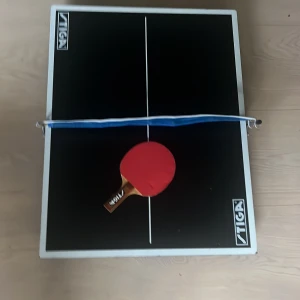 Stiga Mini Pingisbord med Racket och Nät - Kompakt pingisbord från Stiga, perfekt för hemmet. Bordet är i gott skick med tydliga linjer och stabil ram. Medföljer ett Stiga-racket och nät. Perfekt för snabba matcher och enkel förvaring. Inga synliga defekter eller större slitage. Finns även extra nät.