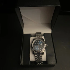 Blå och silver klocka från Parnis - Snygg klocka från seiko med blå urtavla och silverfärgat armband i metall. Klockan har en rund form, räfflad bezel och datumvisning. Länken är klassisk och ger en stilren vibe. Perfekt accessoar för dig som gillar detaljer och vill sticka ut. Även box och länkar ingår.