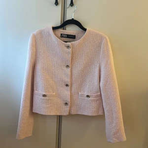 Ljusrosa kavajjacka från Zara XS - Säljer en ljusrosa kavajjacka från Zara i storlek XS. Jackan har en croppad passform, rund halsringning och snygga silvriga knappar framtill. Materialet är strukturerat och känns lyxigt, perfekt för att lyfta vilken outfit som helst.