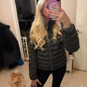 Grön pufferjacka från Colmar  - Säljer en mörkgrön dunjacka från Colmar med huva och diskret logga på ärmen. Storlek 42, passar mig perfekt som är en S/M och får plats med tjocktröjan under. Perfekt för dig som vill ha en snygg och varm jacka med clean look och skön passform.