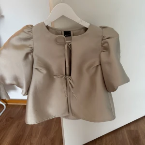 Beige omlottblus från Gina Tricot - Säljer en beige blus från Gina Tricot i storlek XS. Blusen har korta puffärmar och två snygga knytband framtill. 