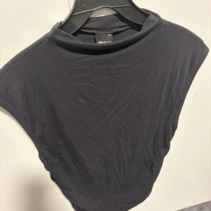 Svart ärmlös topp från Gina Tricot - En svart, enkel och stilren ärmlös topp från Gina Tricot. Toppen har en högre halsringning och är tillverkad i mjukt bomullsmaterial. Perfekt att matcha med jeans eller kjol för en clean look. (Använt 1 gång tidigare) priset kan diskuteras.