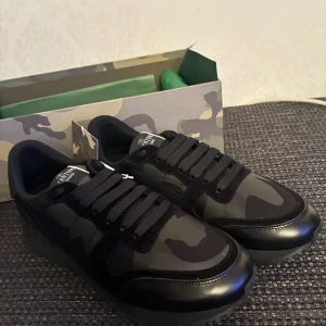 Valentino Garavani Rockrunner sneakers - Svarta Valentino Garavani Rockrunner sneakers med camouflagemönster. Snygg design med platt sula, rund tå och snörning. Materialmix av skinn och syntet ger en cool look. Kommer med originalkartong och dustbag.