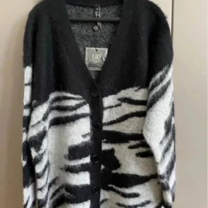Svart och vit zebramönstrad kofta GD - Snygg oversized kofta från GD i svart och vit med zebramönster. Koftan har v-ringad hals, knappar framtill och är stickad i mjukt material. Perfekt för dig som vill ha en statement piece med coolt mönster och skön passform.