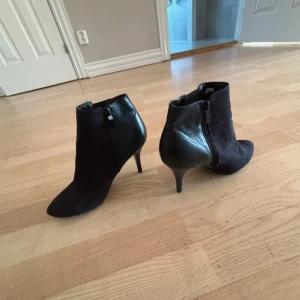 Svarta stövletter med klack och dragkedja - Säljer ett par svarta stövletter med spetsig tå och smal klack. Skorna har en snygg mix av mocka och skinn, samt dragkedja på sidan för enkel påtagning. Perfekta för dig som vill ha en stilren och trendig look.