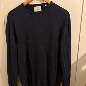 Mörkblå stickad tröja från Bläck - En stilren mörkblå stickad tröja från Bläck i storlek M. Tröjan har rund halsringning och långa ärmar, perfekt för lager-på-lager. Enkel och klassisk design som funkar till många olika outfits.